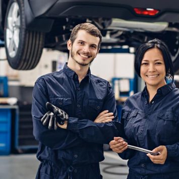 Auto car repair service center. Two happy mechanics - man and woman standing by the car